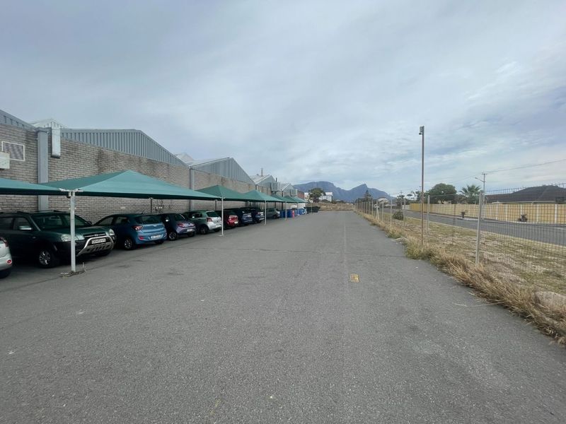 Exterior view of an industrial property featuring a paved parking area with shade cloth carports and perimeter chain link fencing.