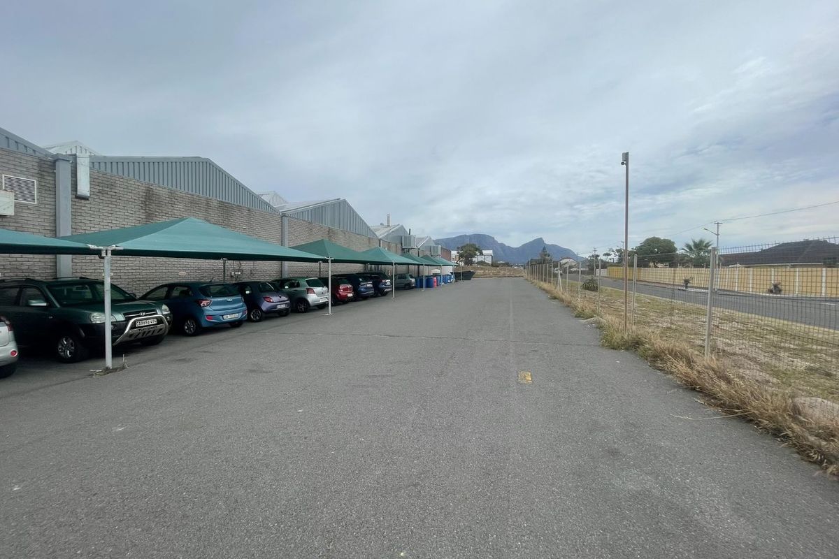 Exterior view of an industrial property featuring a paved parking area with shade cloth carports and perimeter chain link fencing.