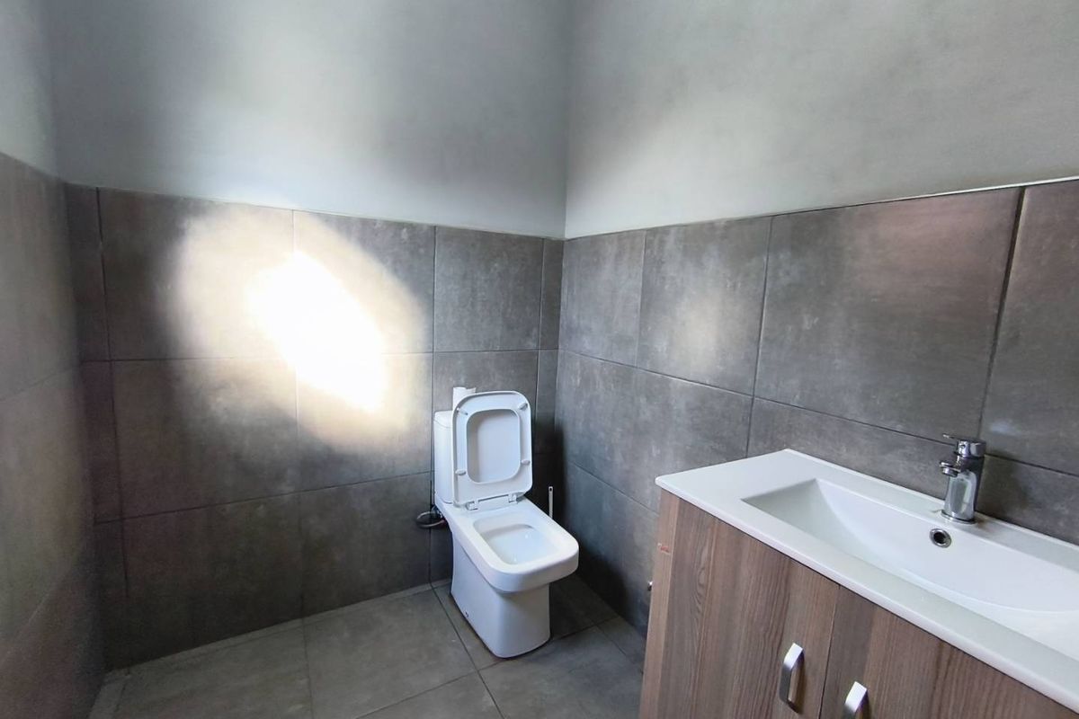 A modern bathroom featuring grey tiled walls and flooring, a white toilet, and a vanity cabinet with an integrated basin.