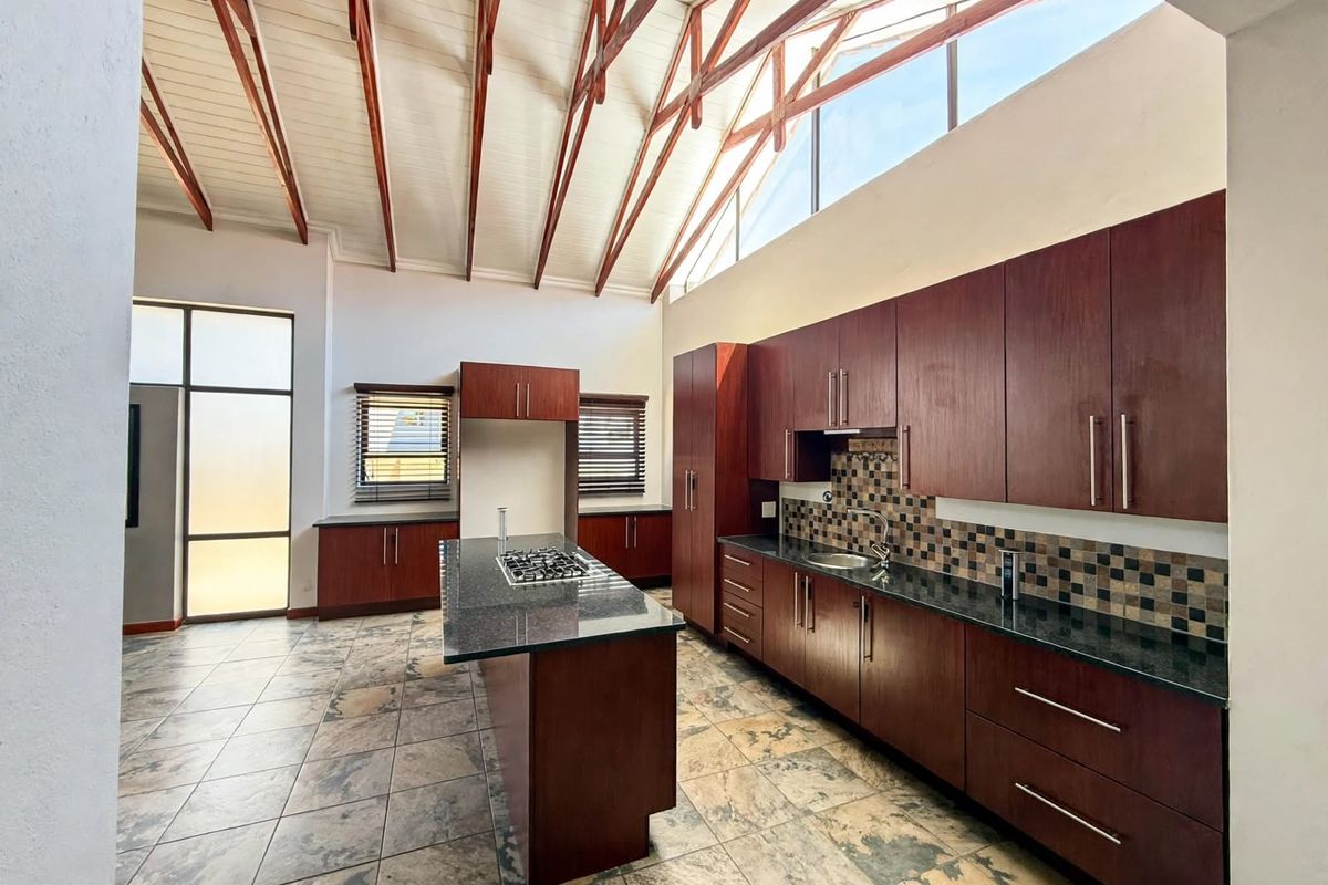 Spacious kitchen featuring dark wood cabinetry, granite countertops, a central island with a gas hob, and a striking vaulted ceiling with exposed timber trusses.