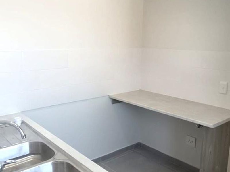 A clean and functional laundry area featuring a double stainless steel sink, laminate countertop, and neutral tiled finishes.