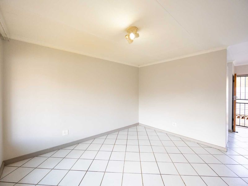 A bright, empty living area featuring neutral tiled flooring and a simple ceiling light fixture, providing a clean canvas for interior design.