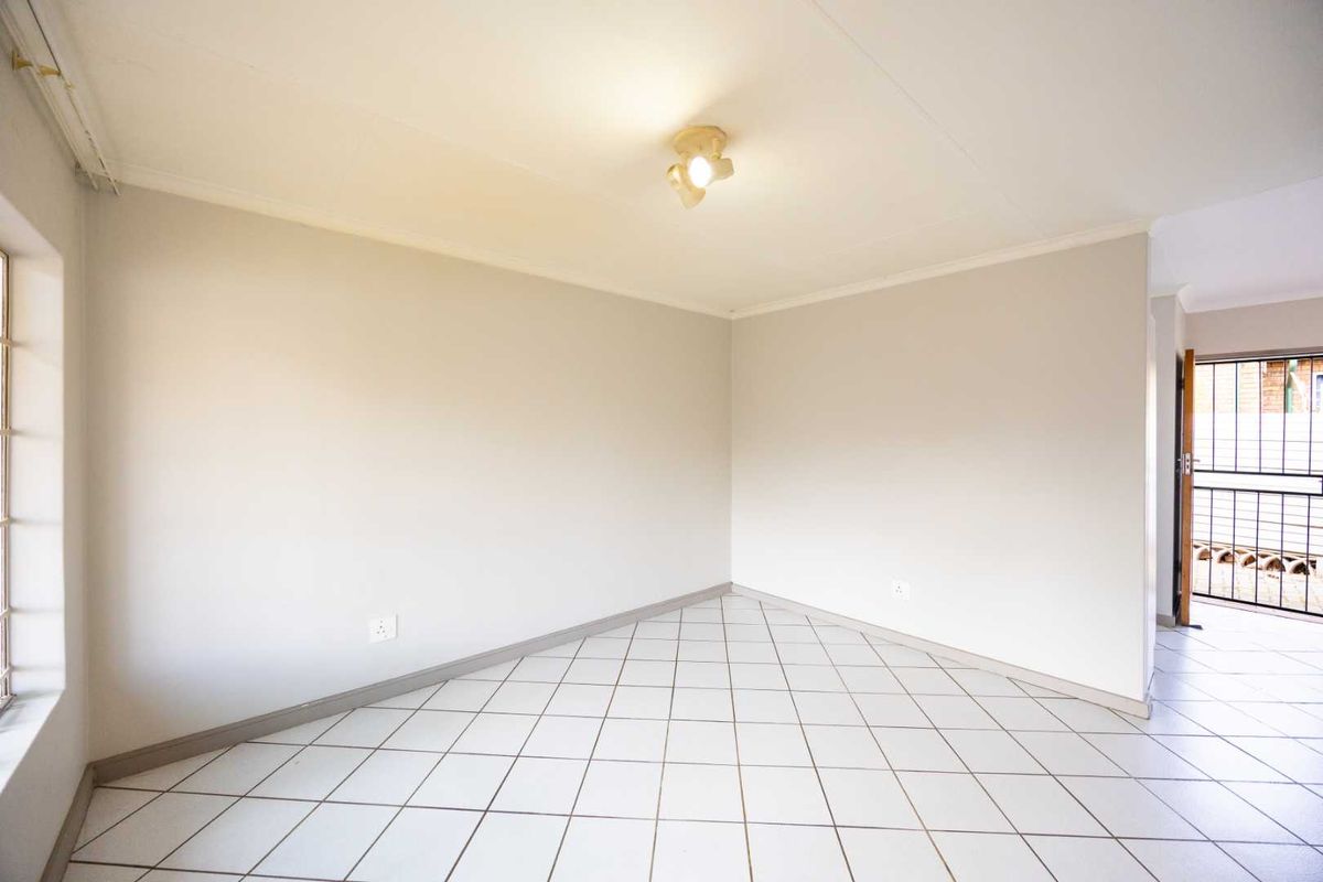 A bright, empty living area featuring neutral tiled flooring and a simple ceiling light fixture, providing a clean canvas for interior design.