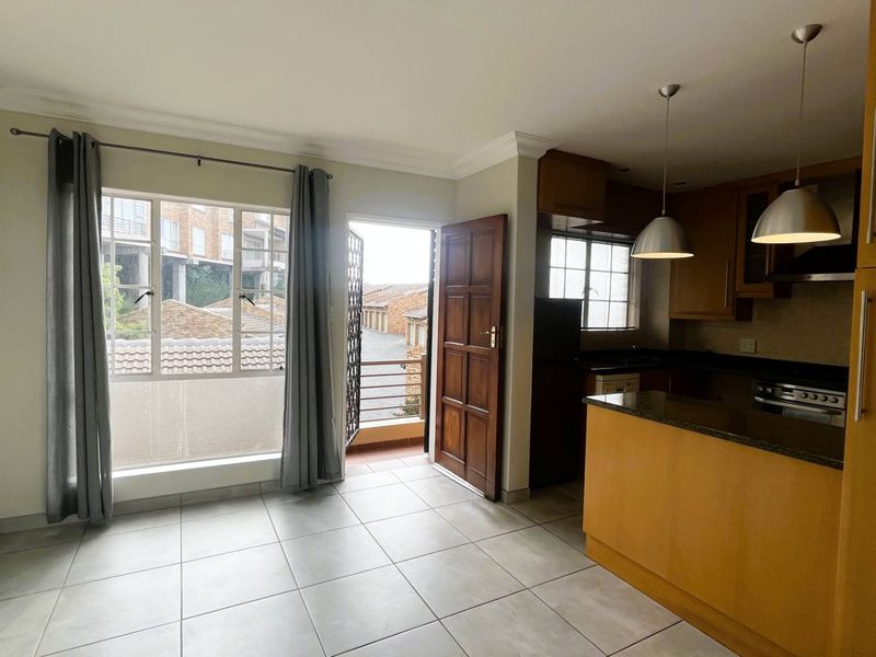 Open-plan living and kitchen area featuring tiled floors, wooden cabinetry, granite countertops, and direct access to a balcony.