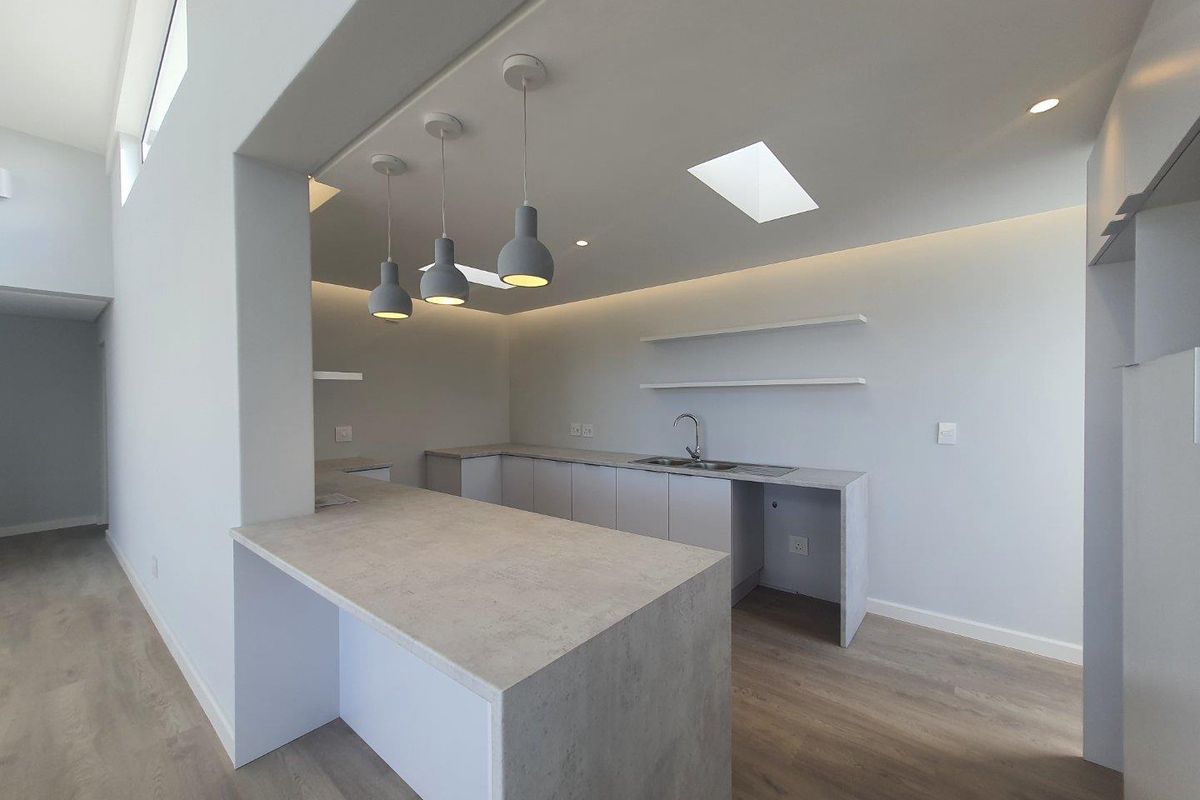 Modern open-plan kitchen featuring stone-look countertops, integrated cabinetry, floating shelves, and contemporary pendant lighting with a skylight above.