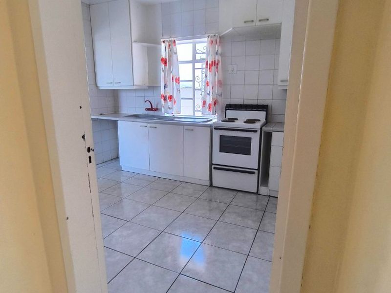A functional kitchen featuring white cabinetry, tiled flooring, a tiled backsplash, and a freestanding stove, viewed from an adjacent hallway.