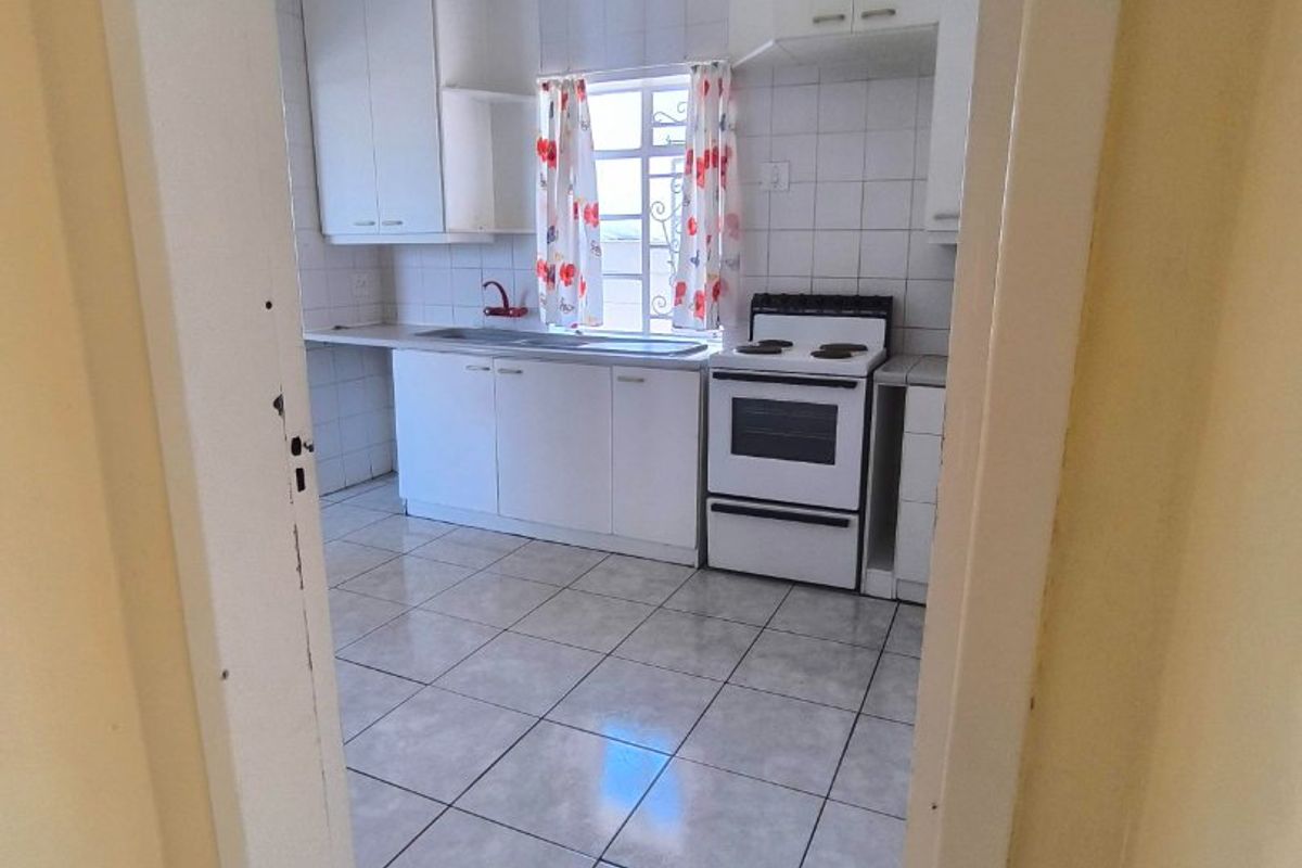A functional kitchen featuring white cabinetry, tiled flooring, a tiled backsplash, and a freestanding stove, viewed from an adjacent hallway.