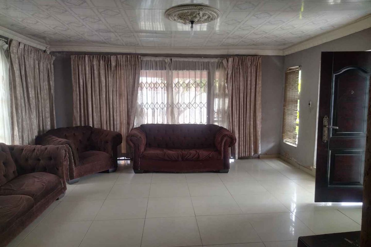 A spacious living room featuring tiled flooring, a decorative ceiling rose, and large windows with security gates.