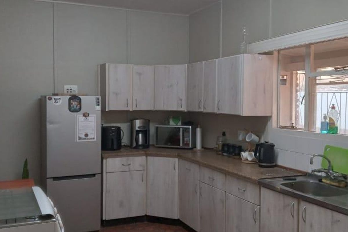 A functional kitchen featuring light wood-grain cabinetry, laminate countertops, a stainless steel sink, and tiled splashbacks with a window overlooking the exterior.