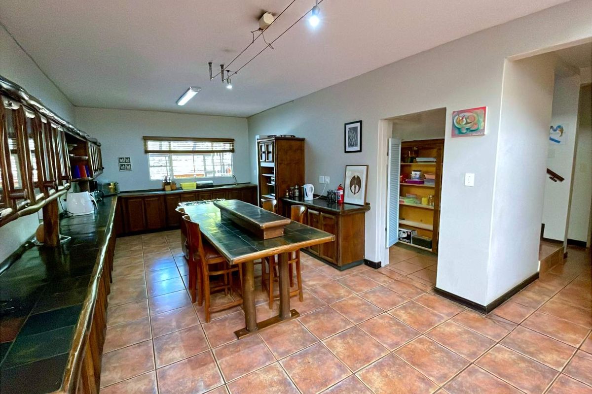Spacious kitchen featuring extensive wooden cabinetry, tiled countertops, and a central island, with an adjacent pantry area and practical tiled flooring throughout.
