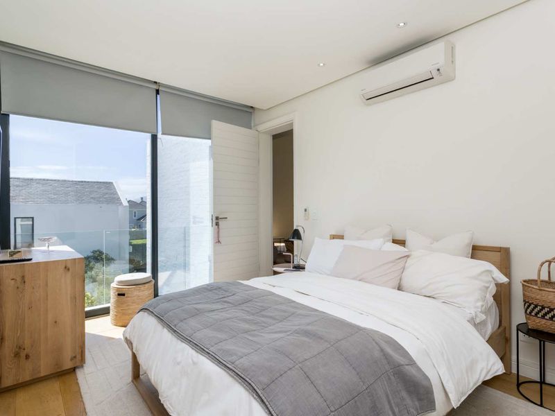 Modern bedroom featuring timber flooring, split-system air conditioning, and floor-to-ceiling glass doors opening to a balcony with a glass balustrade.