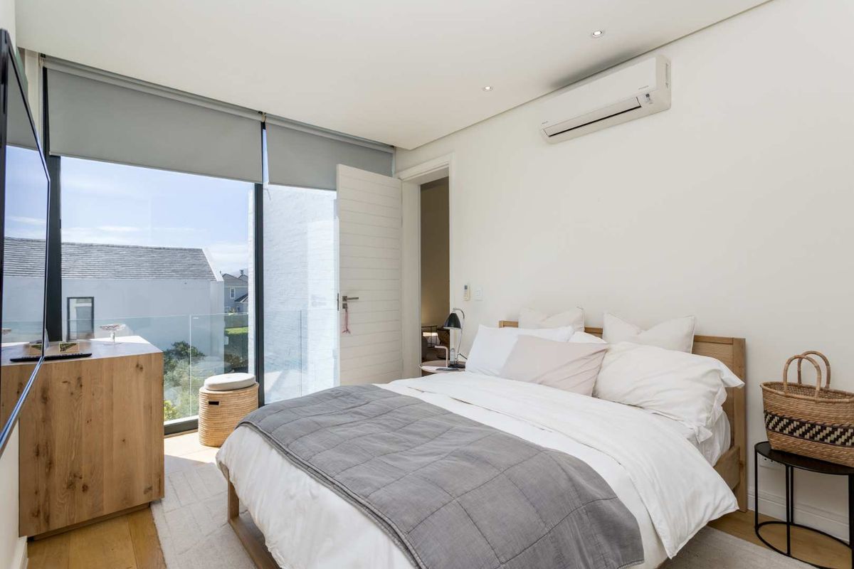 Modern bedroom featuring timber flooring, split-system air conditioning, and floor-to-ceiling glass doors opening to a balcony with a glass balustrade.
