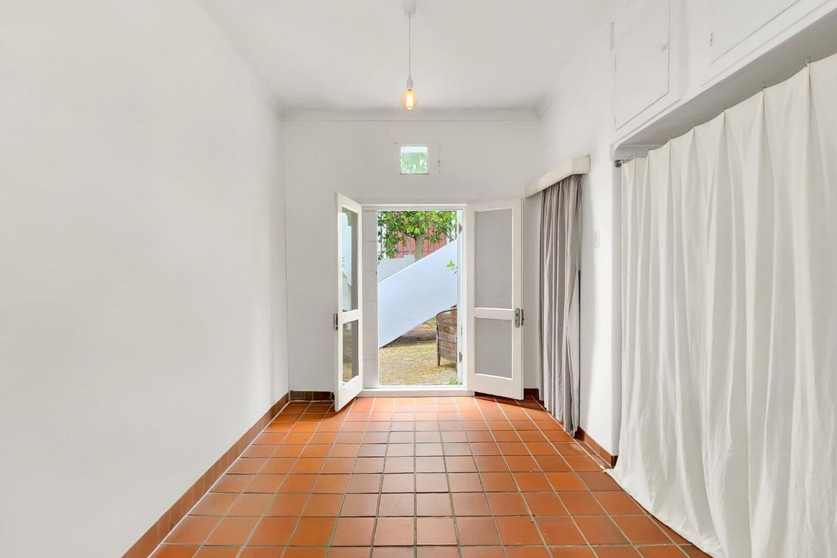 A bright, empty living space featuring terracotta floor tiles, built-in storage cupboards, and direct access to an outdoor area through double french doors.