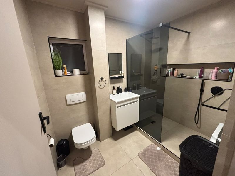 Modern bathroom featuring a walk-in shower with a glass screen, wall-mounted toilet with concealed cistern, and a sleek vanity unit with neutral tiling.