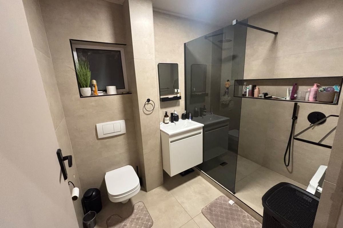 Modern bathroom featuring a walk-in shower with a glass screen, wall-mounted toilet with concealed cistern, and a sleek vanity unit with neutral tiling.