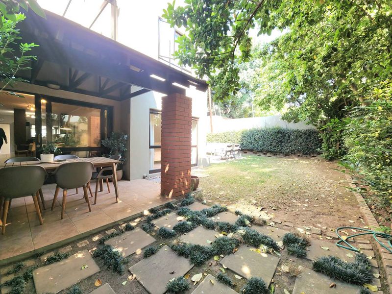 A covered patio area featuring tiled flooring and a brick pillar, seamlessly connecting to a private garden with paved pathways.