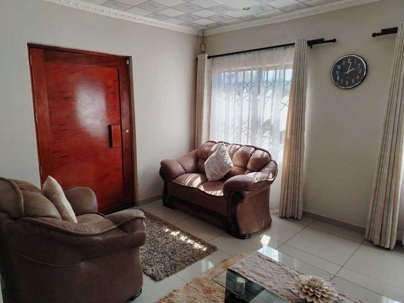 A living room featuring tiled flooring, a solid timber door, and decorative ceiling tiles, providing a functional space with natural light.