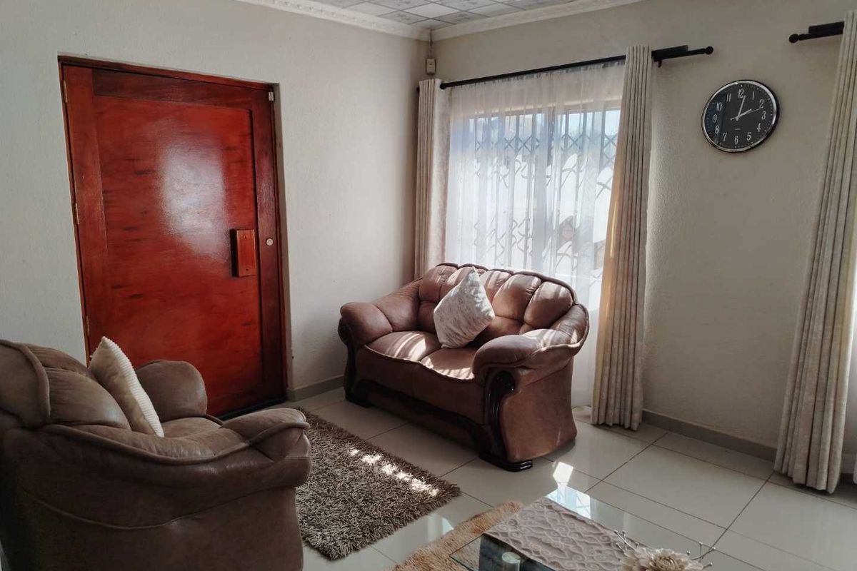 A living room featuring tiled flooring, a solid timber door, and decorative ceiling tiles, providing a functional space with natural light.