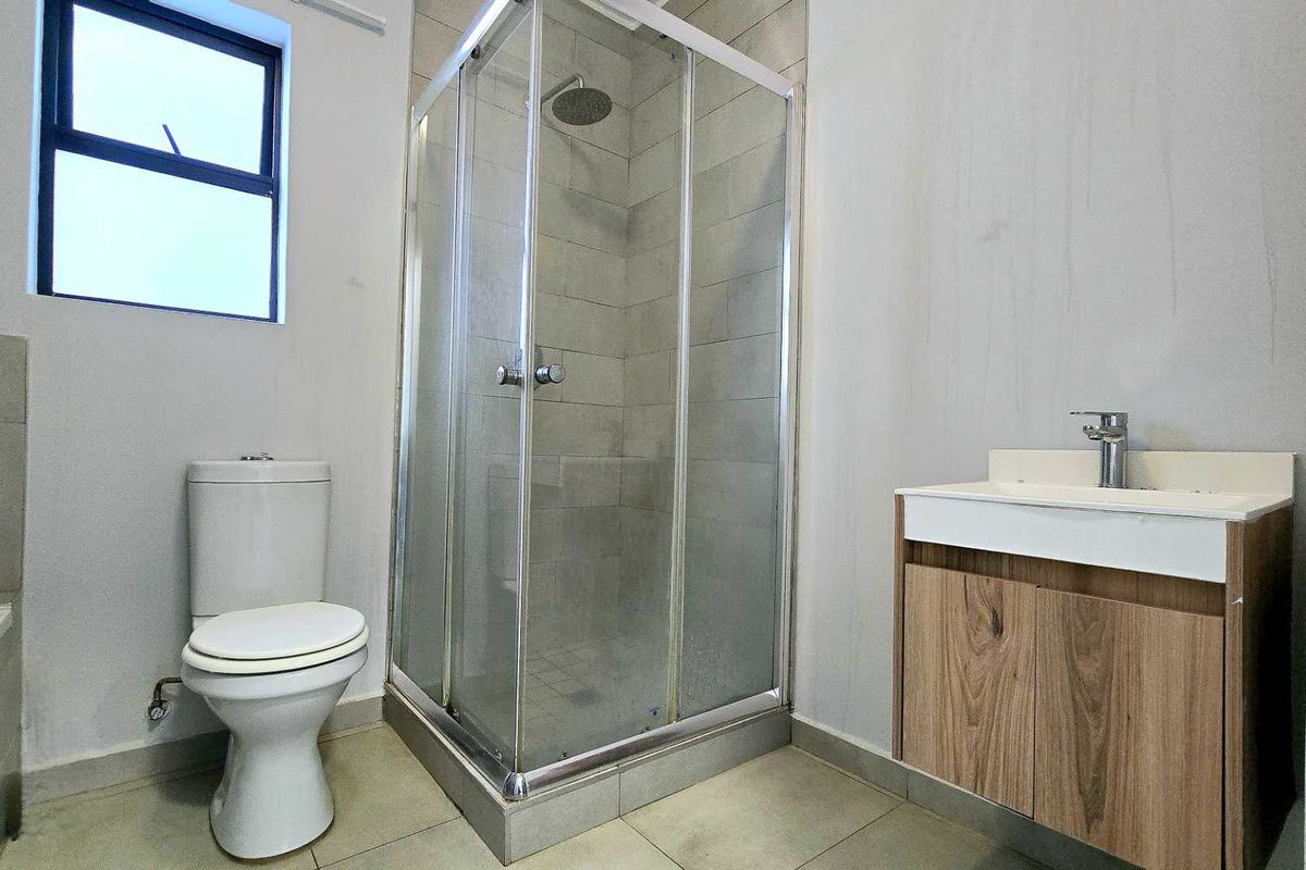 A functional bathroom featuring a glass shower enclosure, a modern vanity with a washbasin, and a standard toilet, finished with neutral floor tiles.