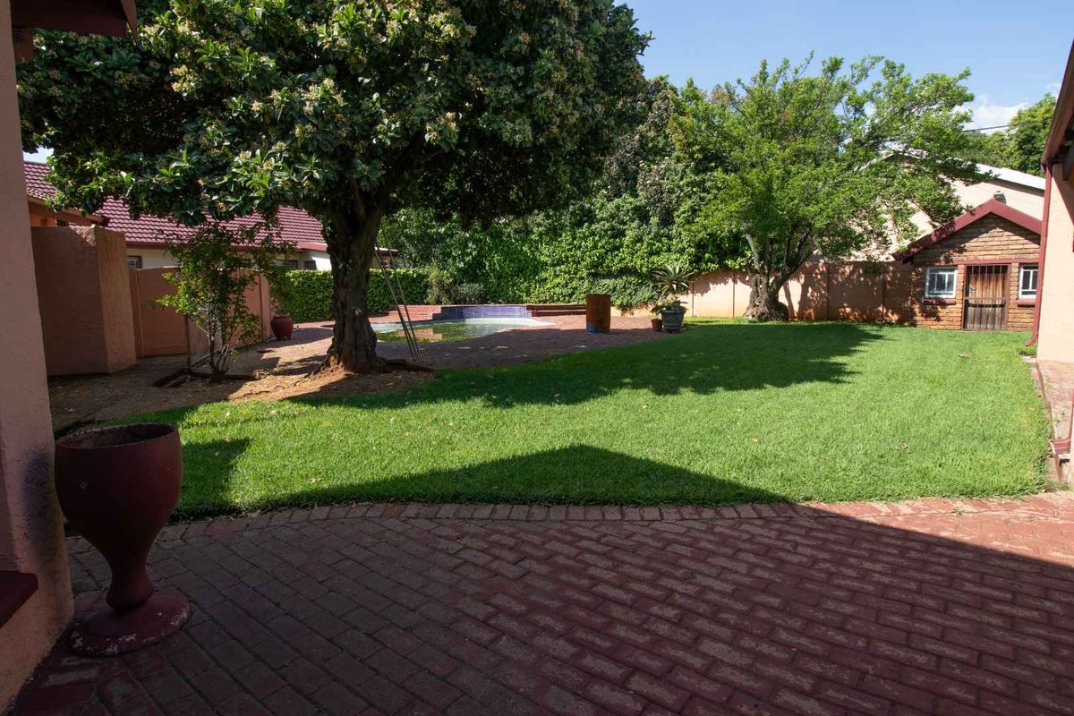 Spacious rear garden featuring a swimming pool, brick paved patio area, established lawn, mature trees, and a small brick outbuilding.