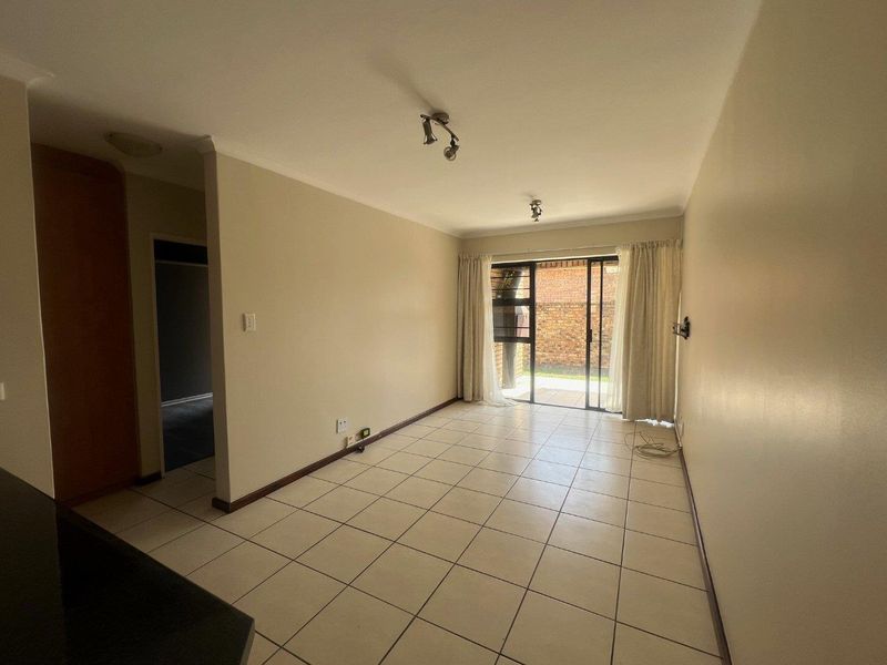 A bright, empty living room featuring neutral tiled flooring and a sliding glass door providing access to the outdoor area.