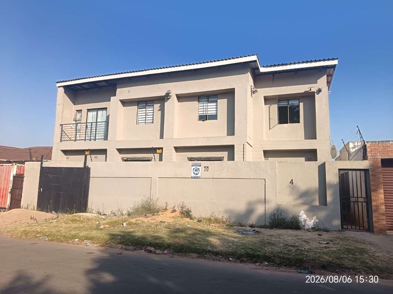 Two-story residential property featuring a perimeter wall with electric fencing, security gates, and a balcony, presenting a secure street-facing facade.