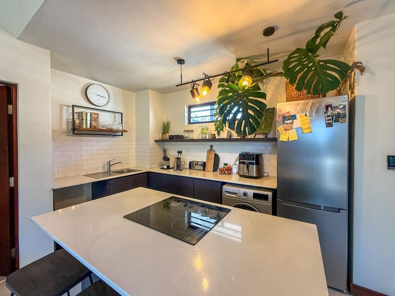 Modern kitchen featuring a central island with an induction cooktop, subway tile backsplash, quartz countertops, and sleek dark cabinetry.