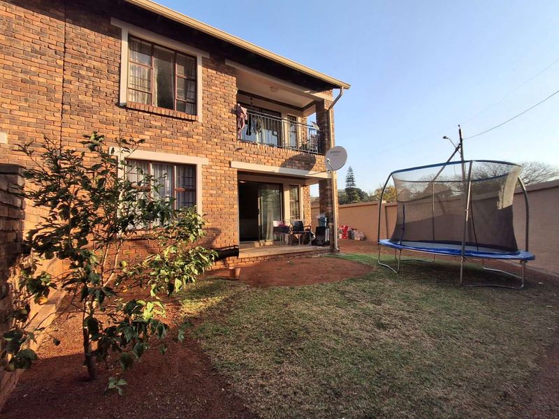 Rear view of a two-story face brick apartment building featuring a ground-level patio, upper-level balcony with metal railing, and a private garden area.