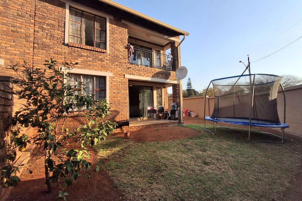 Rear view of a two-story face brick apartment building featuring a ground-level patio, upper-level balcony with metal railing, and a private garden area.