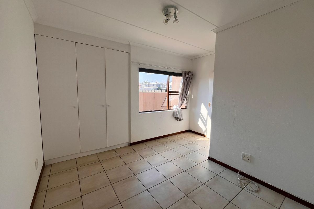 A bright, empty bedroom featuring tiled flooring, built-in cupboards, and a window providing natural light.