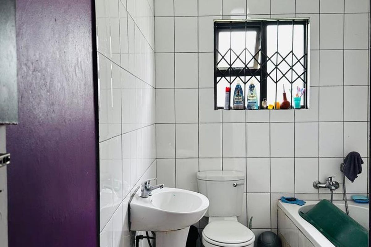 A compact bathroom featuring a pedestal basin, toilet, and bathtub with tiled walls and security bars on the window.
