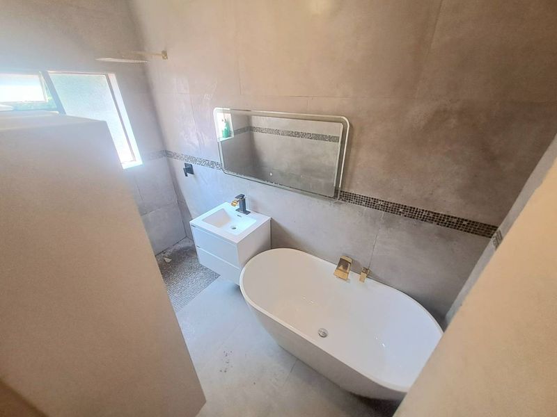 Modern bathroom featuring a sleek freestanding bathtub, wall-mounted vanity, and contemporary gold-tone fixtures against neutral tiled walls.
