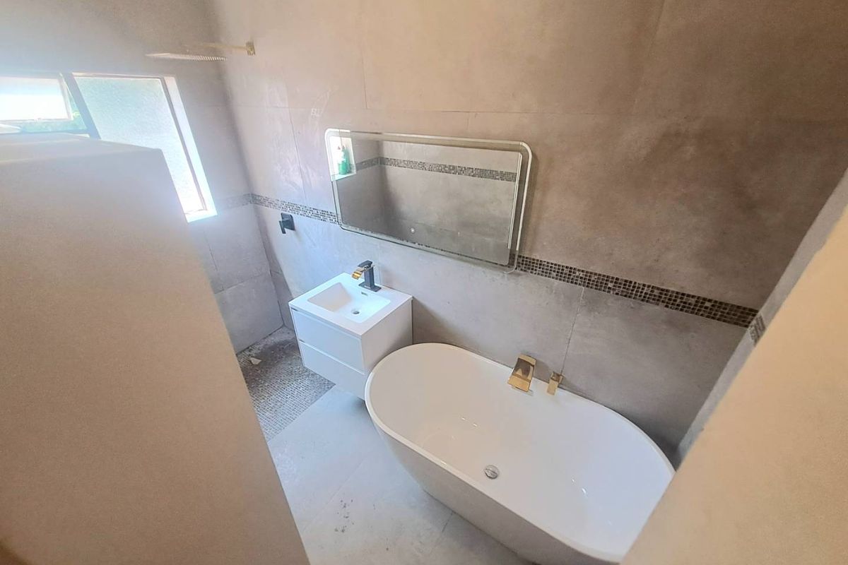 Modern bathroom featuring a sleek freestanding bathtub, wall-mounted vanity, and contemporary gold-tone fixtures against neutral tiled walls.