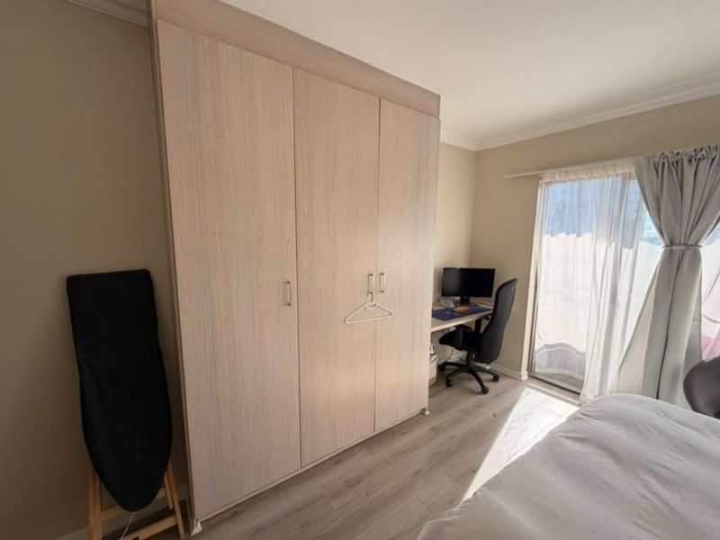A well-maintained bedroom featuring light wood-tone built-in wardrobes, modern laminate flooring, and a sliding glass door providing natural light.