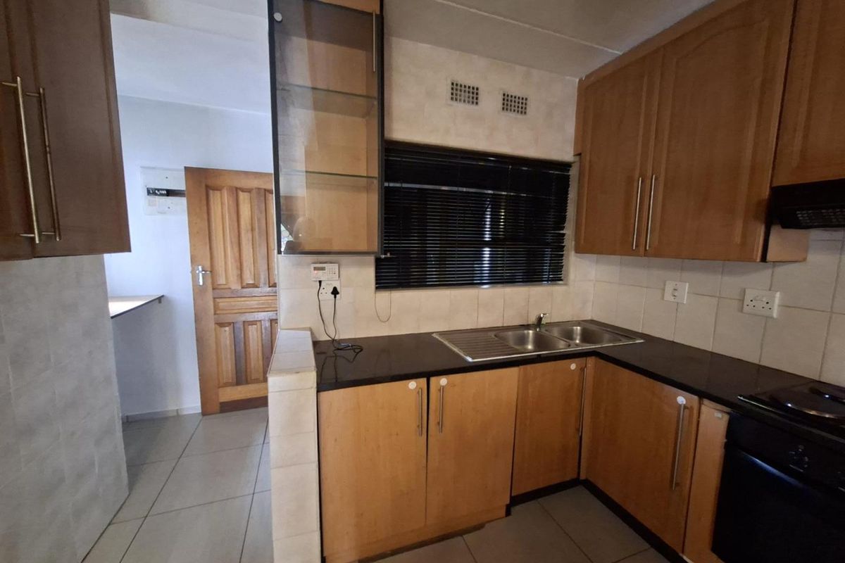 Functional kitchen featuring wood-veneer cabinetry, dark granite countertops, stainless steel double sink, and integrated oven with hob.