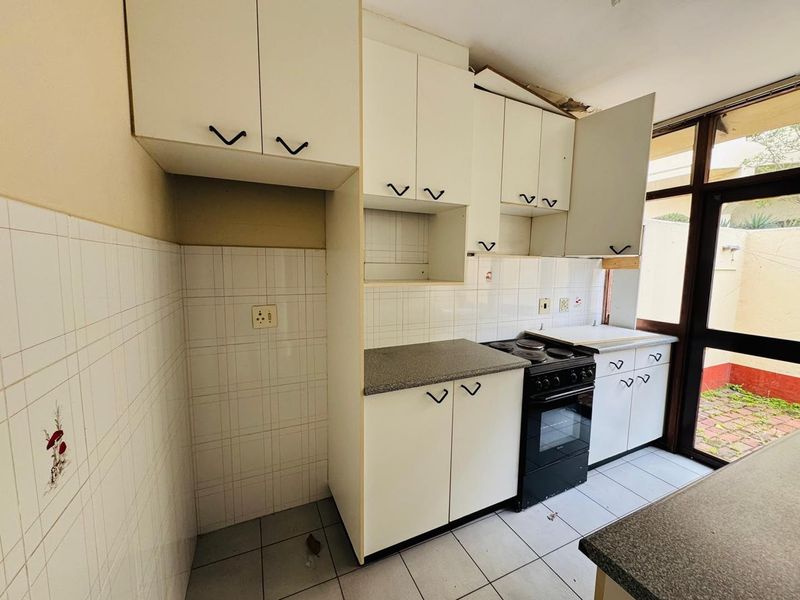 A dated kitchen featuring built-in cabinetry, a freestanding stove, and tiled surfaces, requiring renovation to modernize the space.