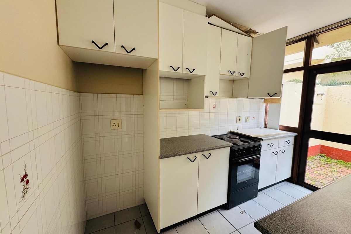 A dated kitchen featuring built-in cabinetry, a freestanding stove, and tiled surfaces, requiring renovation to modernize the space.