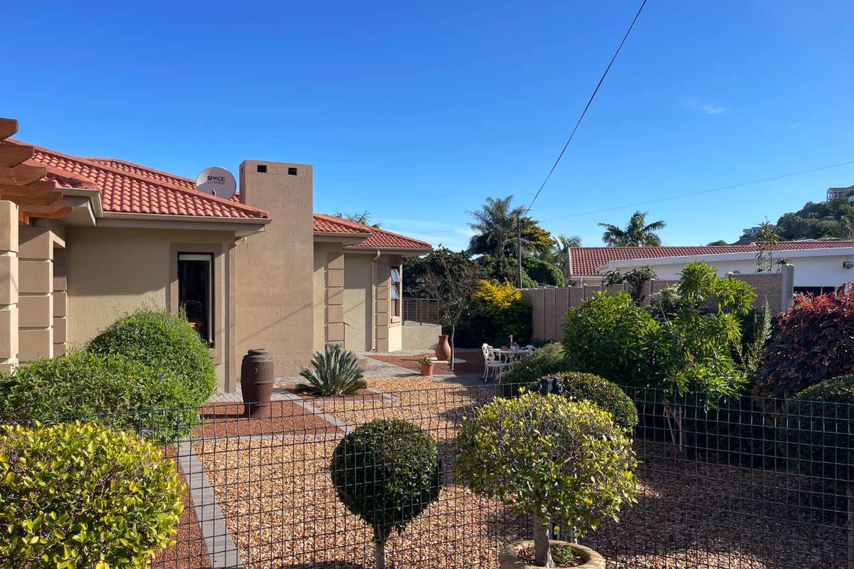 A well-maintained rear garden area featuring a paved walkway, established landscaping, and a clear view of the home's exterior facade and terracotta roof.