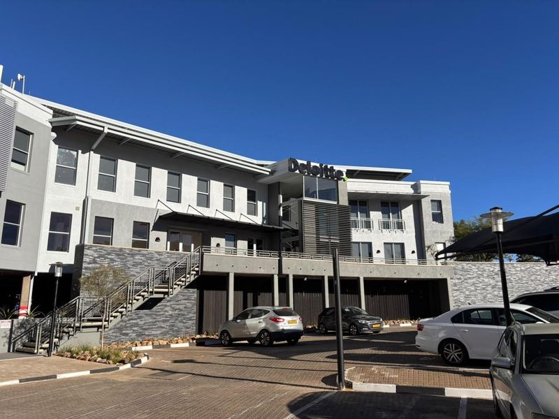 Front elevation of a modern office building featuring stone cladding, metal architectural details, and a paved parking area.