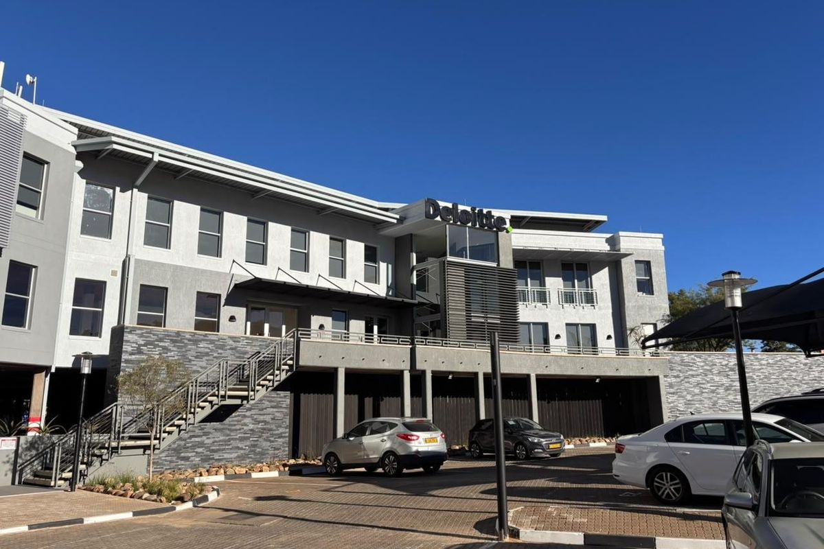 Front elevation of a modern office building featuring stone cladding, metal architectural details, and a paved parking area.