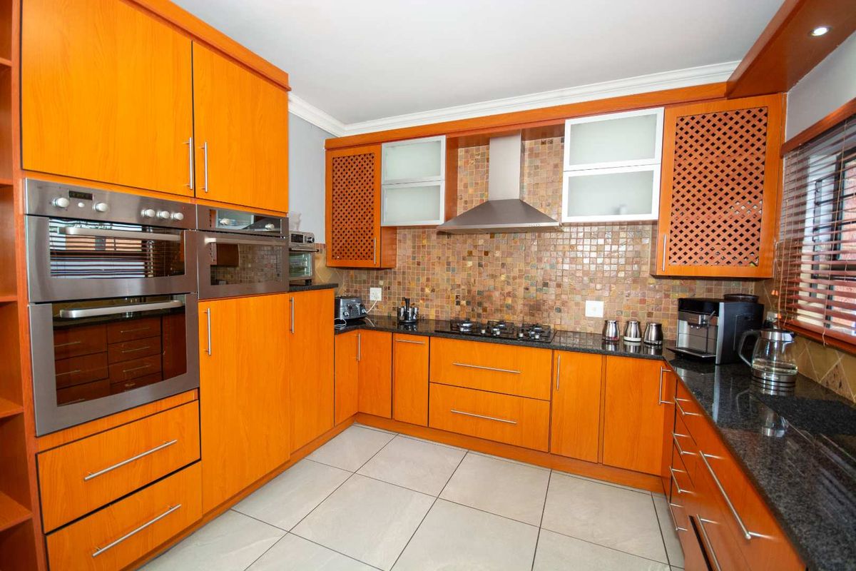 A functional kitchen featuring warm-toned wooden cabinetry, granite countertops, a mosaic tile backsplash, and built-in stainless steel appliances including an oven and gas hob.