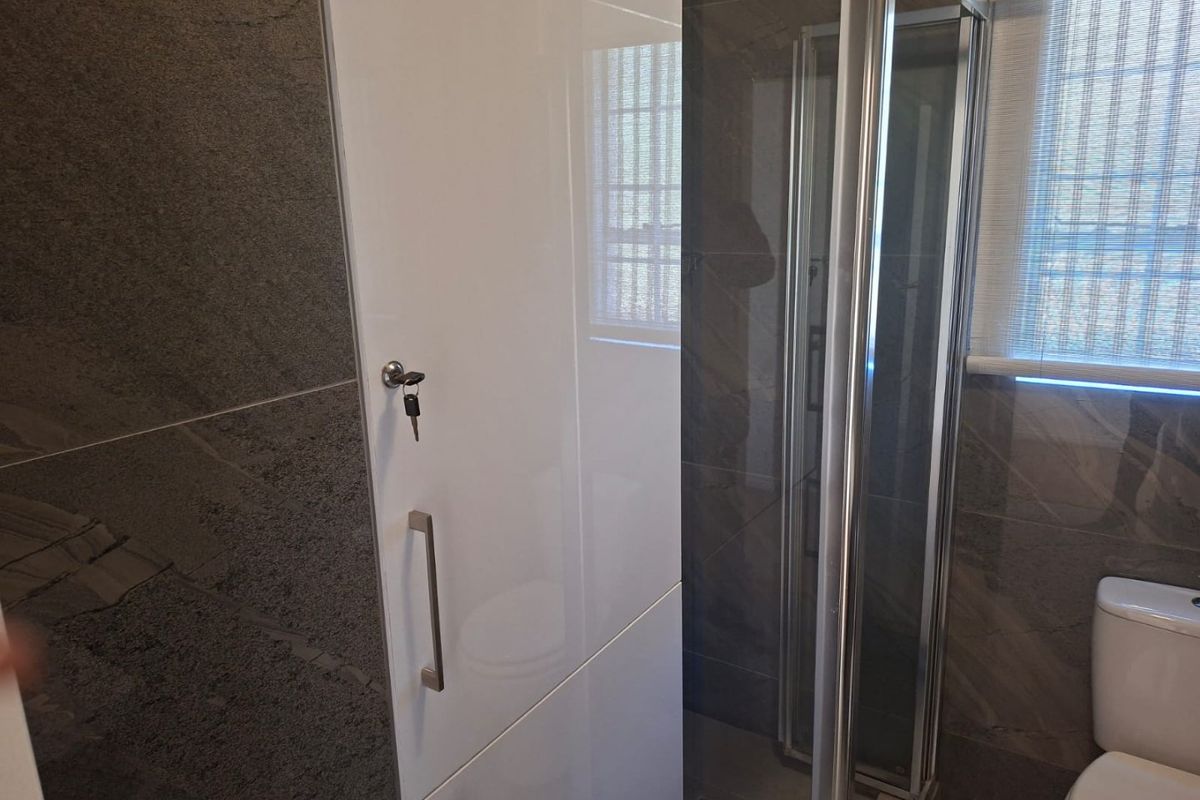 Modern bathroom featuring a glass shower enclosure, white built-in cabinetry, and dark grey wall tiling.
