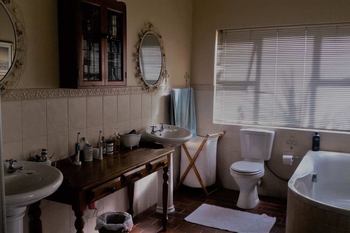 A functional bathroom featuring a pedestal basin, a built-in bathtub, and a toilet, with neutral wall tiles and a window providing natural light.
