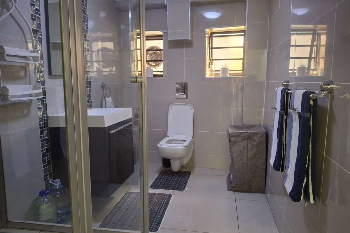 A modern bathroom featuring a wall-mounted toilet, a vanity with integrated basin, and a glass-enclosed shower with tiled walls.