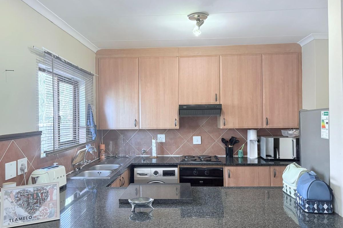 A functional kitchen featuring light wood cabinetry, dark granite countertops, a built-in oven, hob, extractor fan, and a double stainless steel sink.