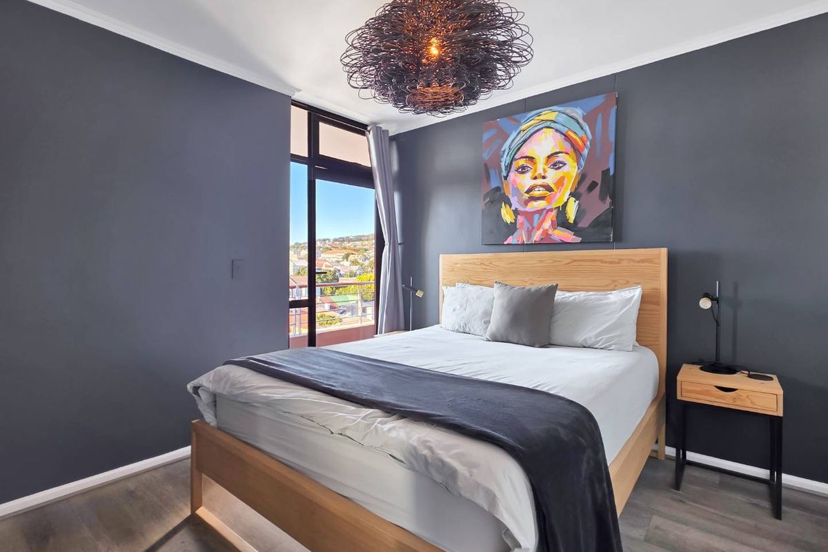 A well-maintained bedroom featuring dark accent walls, laminate flooring, and a sliding glass door providing access to an outdoor balcony with neighborhood views.