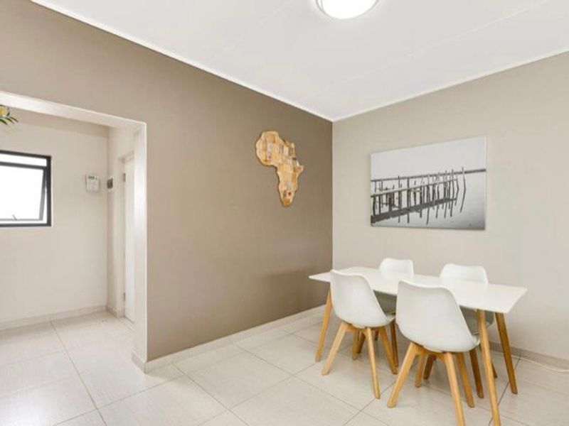 A bright dining area featuring neutral wall tones, tiled flooring, and a functional layout with access to an adjacent hallway.