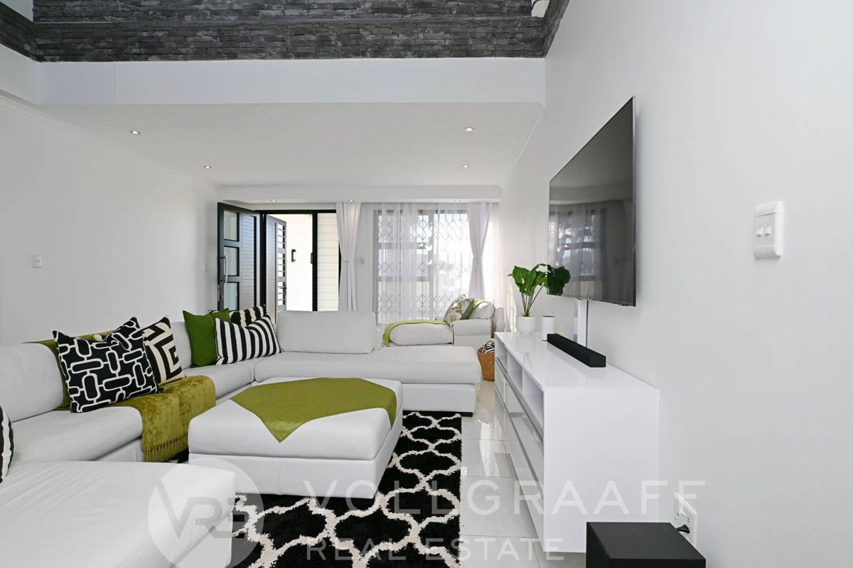 Modern living room featuring high ceilings with stone-cladding detail, recessed lighting, and large glass doors leading to an outdoor area.