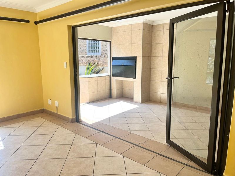 Covered patio area featuring tiled flooring, built-in braai, and aluminium stack doors providing seamless indoor-outdoor flow.