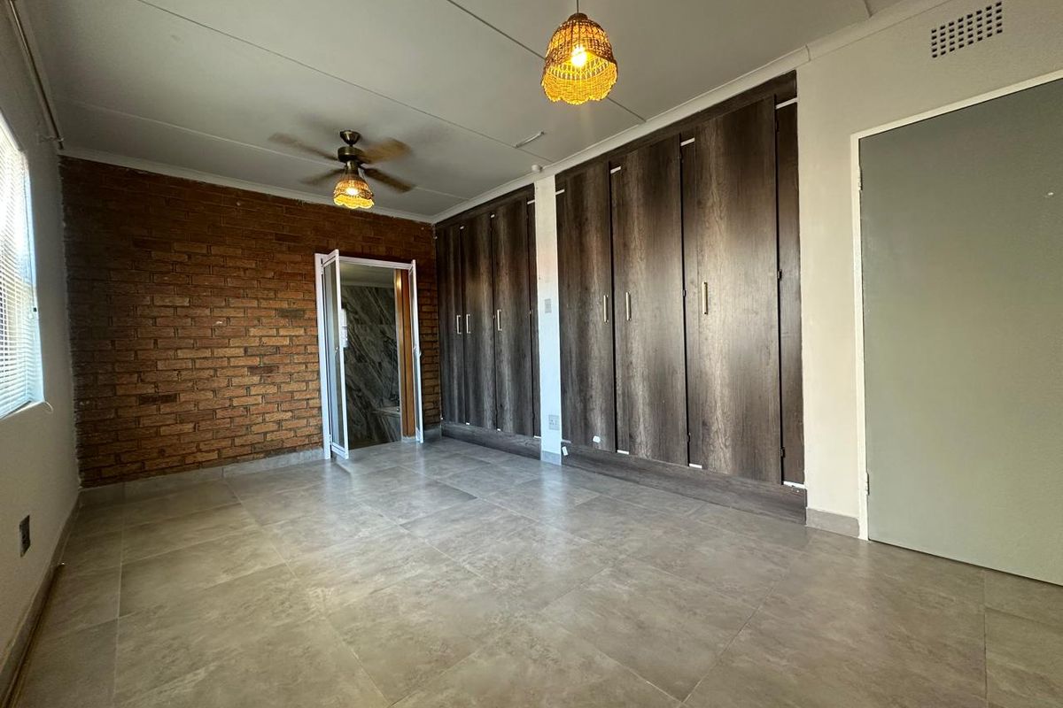 Spacious bedroom featuring modern tiled flooring, an exposed brick feature wall, and extensive built-in cupboard storage.